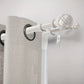 Curtain rod with decorative finials and gray curtains on a plain background