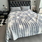 Gray and white plaid blanket draped over a bed in a bedroom setting.