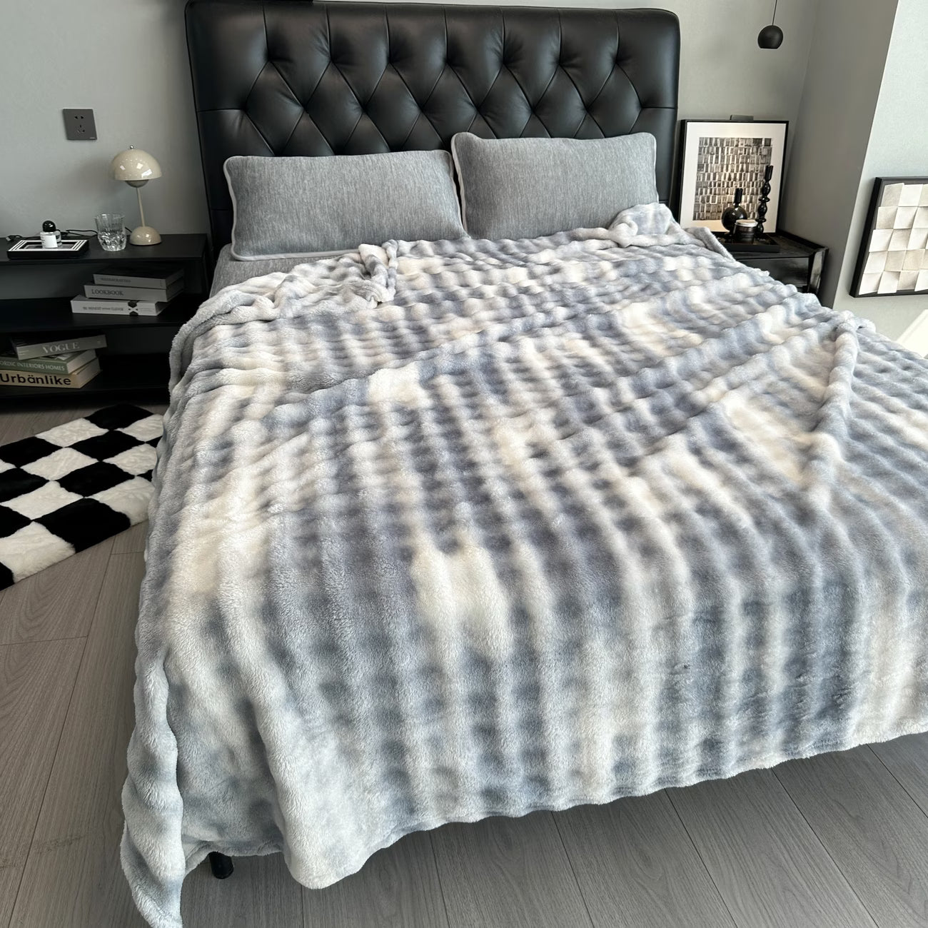 Gray and white plaid blanket draped over a bed in a bedroom setting.