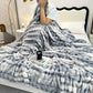 Person wrapped in a fluffy gray blanket on a bed with a book and mug beside them.
