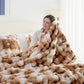 Woman wrapped in a fluffy brown and beige blanket in a cozy bedroom.