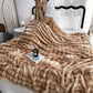 Person wrapped in a fluffy beige blanket on a bed with a candle and book on the nightstand.