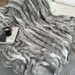 Gray textured blanket draped over a surface with a cup and magazine underneath.