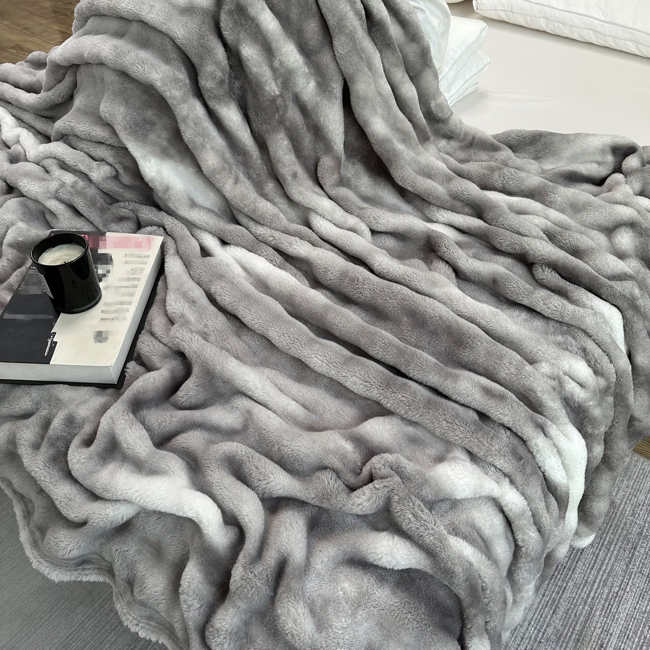 Gray textured blanket draped over a surface with a cup and magazine underneath.