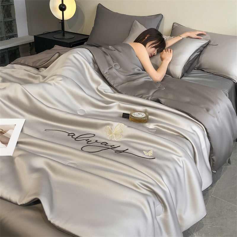 Person lying on a bed with a satin blanket featuring the word 'always' and butterfly designs.