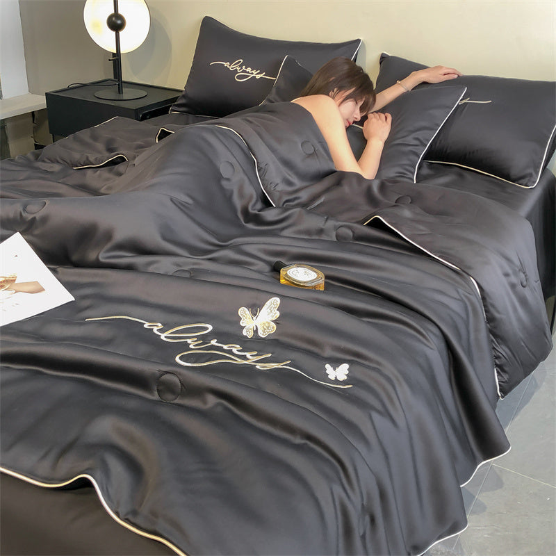 Person lying in bed under a dark gray comforter with 'always' embroidery, in a bedroom setting.