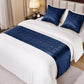 Bed with white bedding and blue decorative pillows and runner in a bedroom setting.