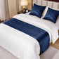 Bed with white bedding and blue decorative runner and pillows in a bedroom setting.