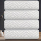 Four white towels with a geometric pattern stacked on a dark surface.