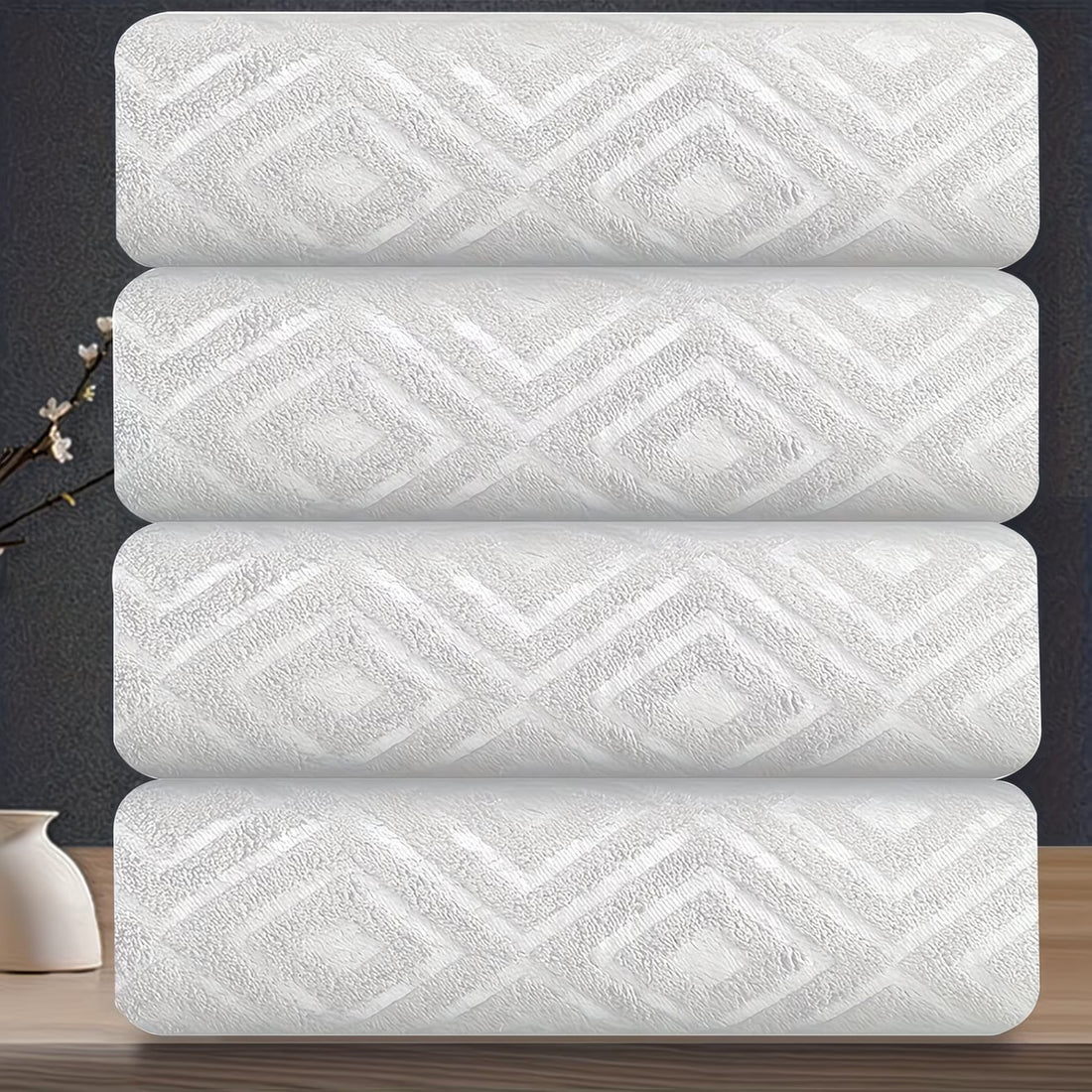 Four white towels with a geometric pattern stacked on a dark surface.
