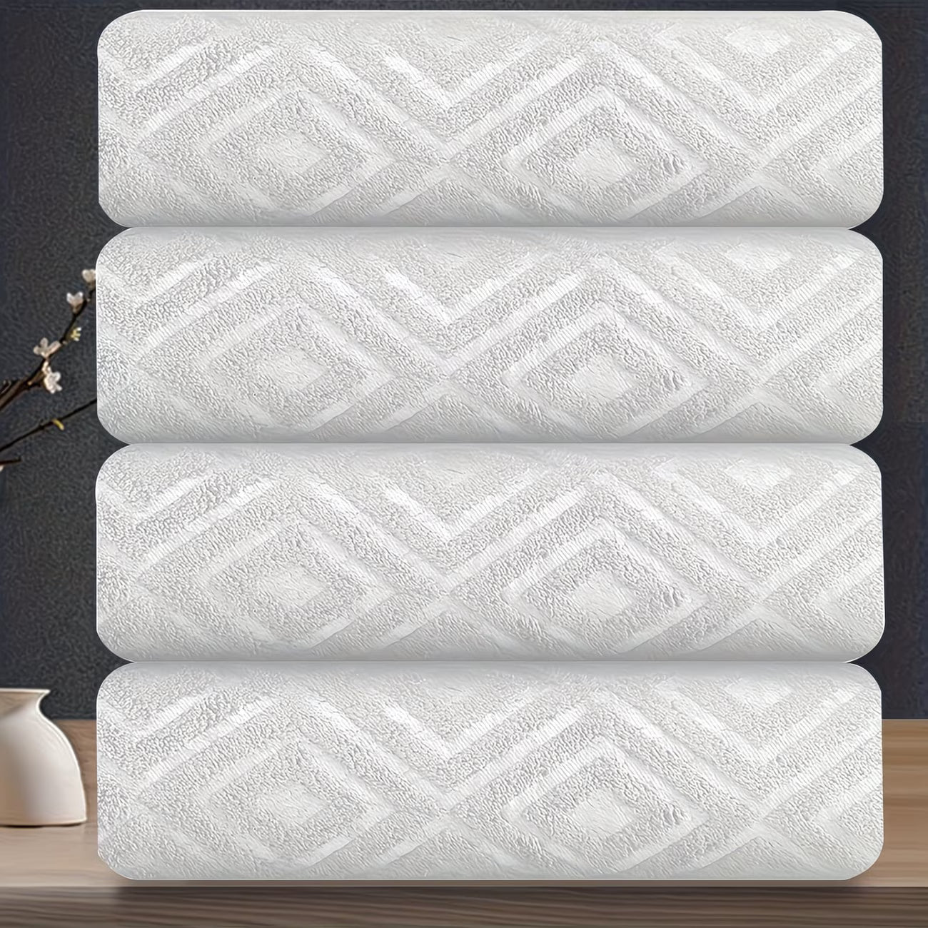 Four white towels with a geometric pattern stacked on a dark surface.