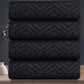 Stack of black towels with geometric pattern on a reflective surface against a dark background