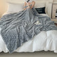 Person wrapped in a gray blanket on a bed with a cup and book in hand
