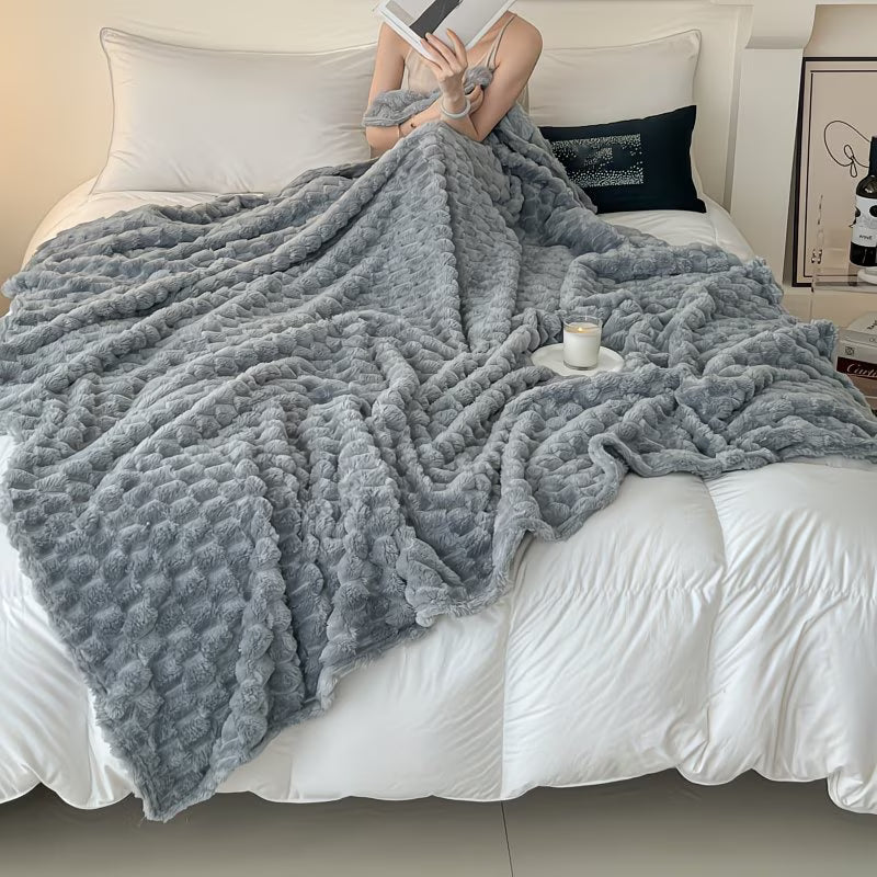 Person wrapped in a gray blanket on a bed with a cup and book in hand