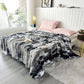 Gray and black tie-dye blanket on a bed in a bright bedroom with pink pillows.