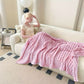 Woman sitting on a couch with a pink blanket, reading a book in a cozy living room.