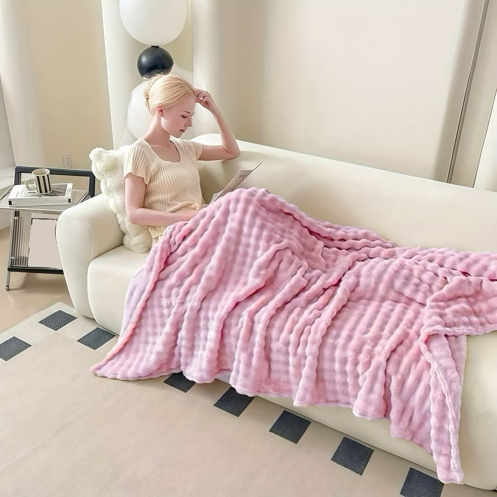 Woman sitting on a couch with a pink blanket, reading a book in a cozy living room.