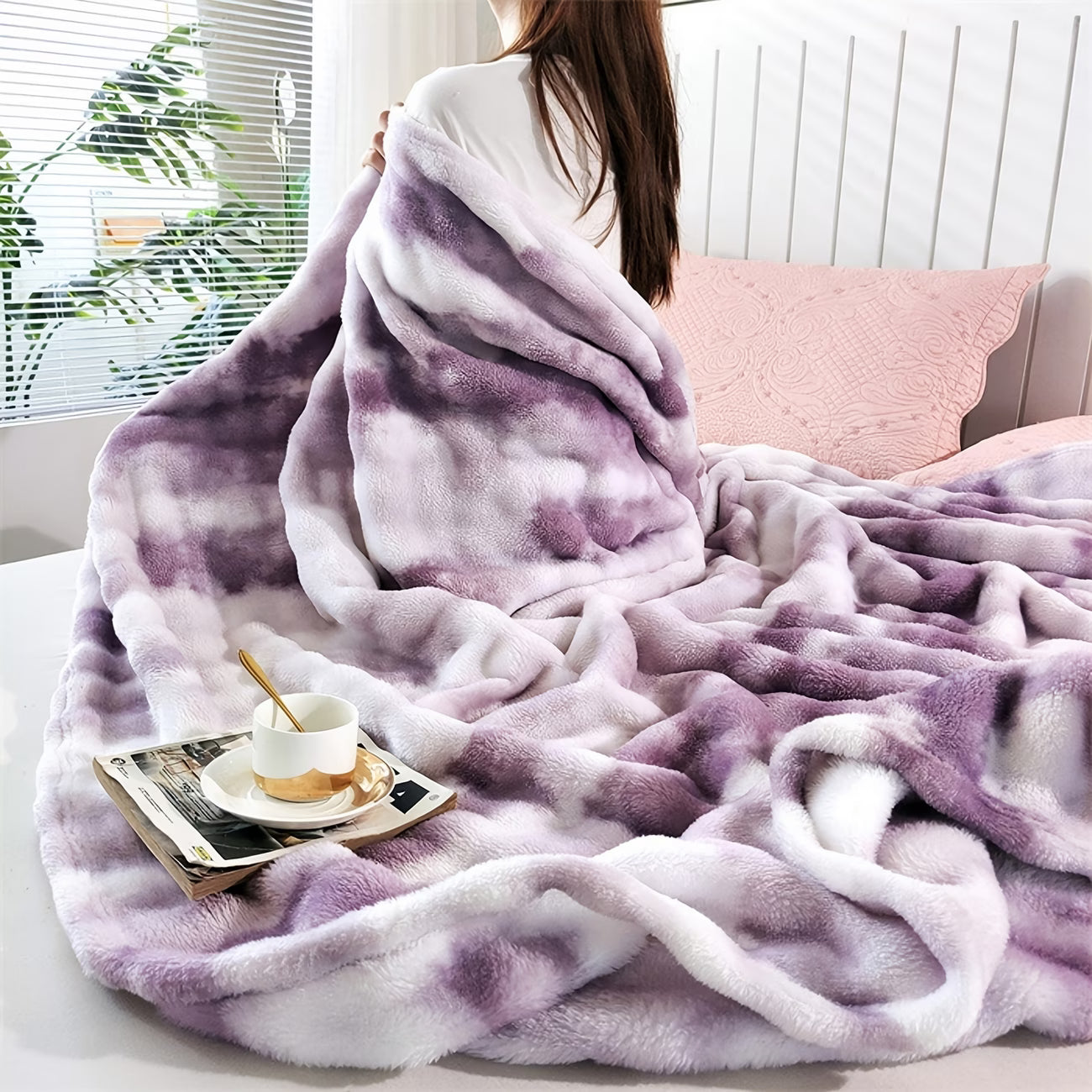 Person wrapped in a purple and white blanket with a tray of tea on a bed.