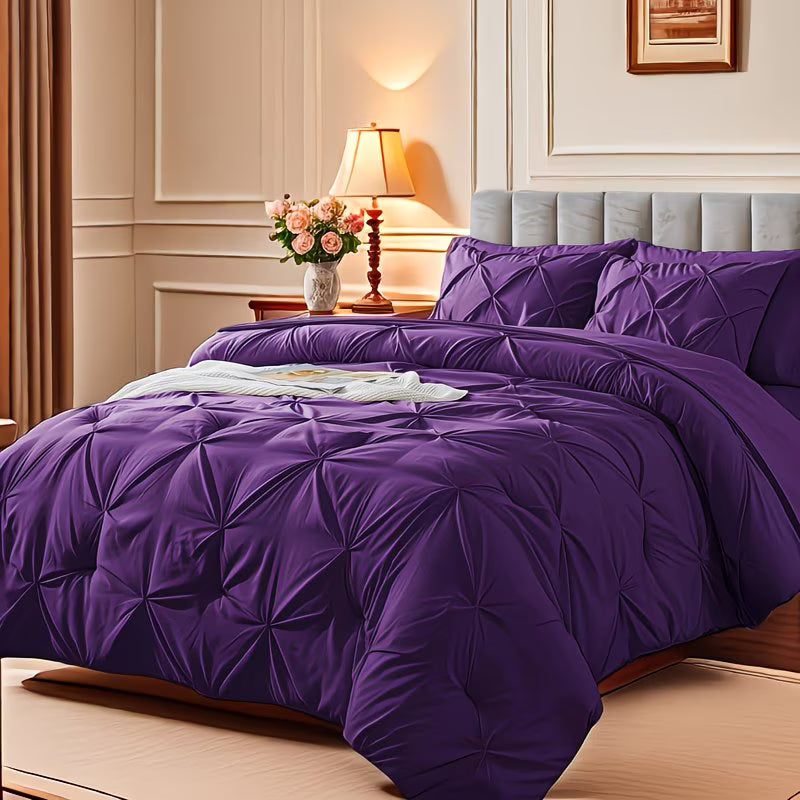 Purple bedspread on a neatly made bed in a bedroom with a lamp and flowers on a nightstand.