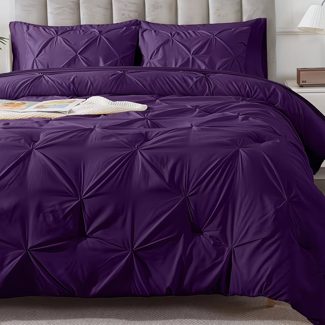 Purple textured comforter set on a bed with pillows and a lamp in the background.