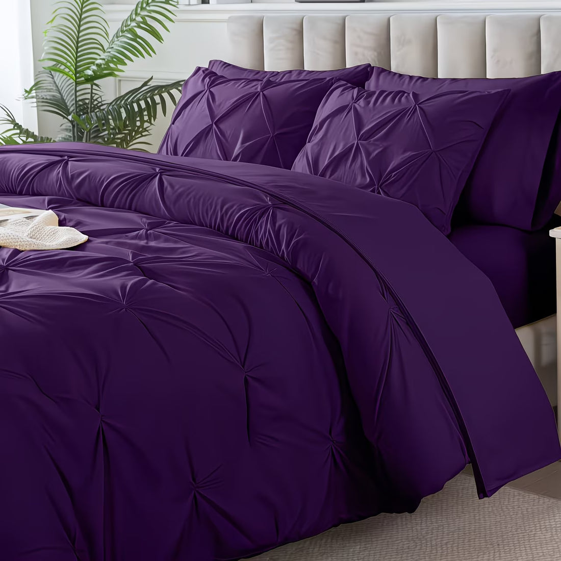 Purple bedding set on a bed with pillows and a plant in the background