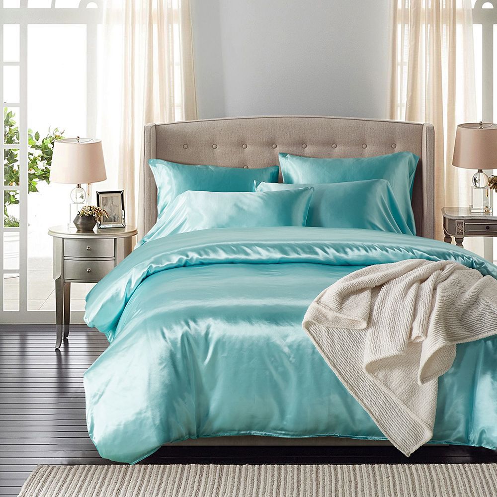 Turquoise bedding set on a bed in a well-lit bedroom with lamps and curtains.