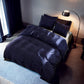 Navy blue bedding set on a bed in a dimly lit bedroom with a lamp and curtains.