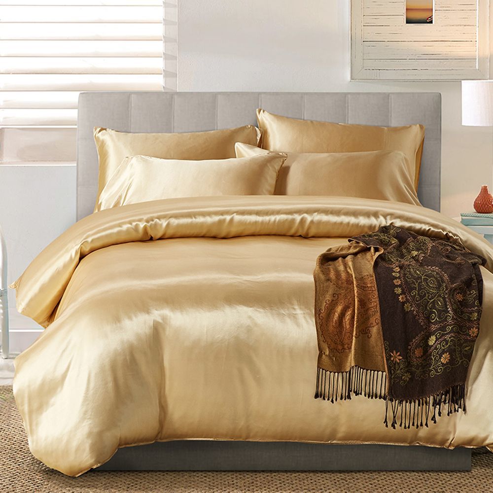 Gold satin bedding set on a bed with a decorative throw blanket in a bedroom setting.