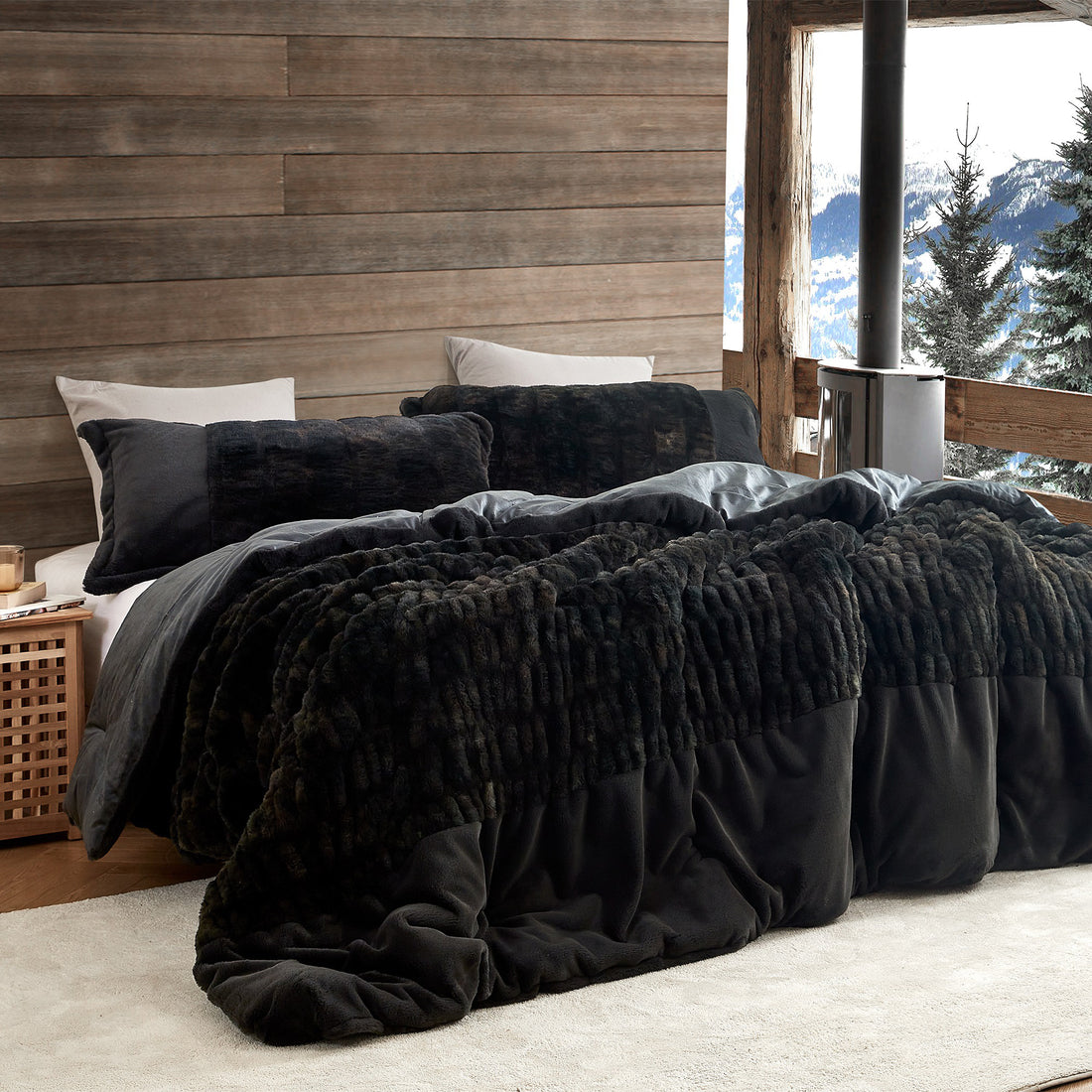 Black textured comforter on a bed with a wooden wall and mountain view in the background