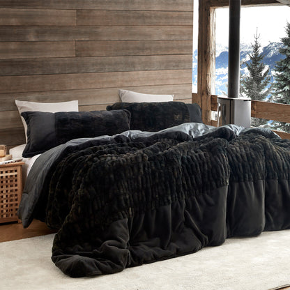 Black textured comforter on a bed with a wooden wall and mountain view in the background