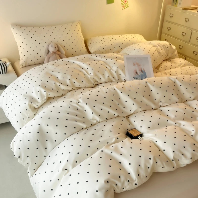 White comforter with black polka dots on a bed in a bedroom setting.