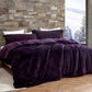 Purple comforter set on a bed with a stone wall and window view in the background