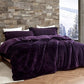 Purple comforter on a bed with a stone wall and window view in the background