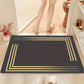 Black doormat with gold border on a wooden floor, person entering through glass door.