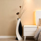 Black and white vase with dried flowers on a nightstand next to a bed.