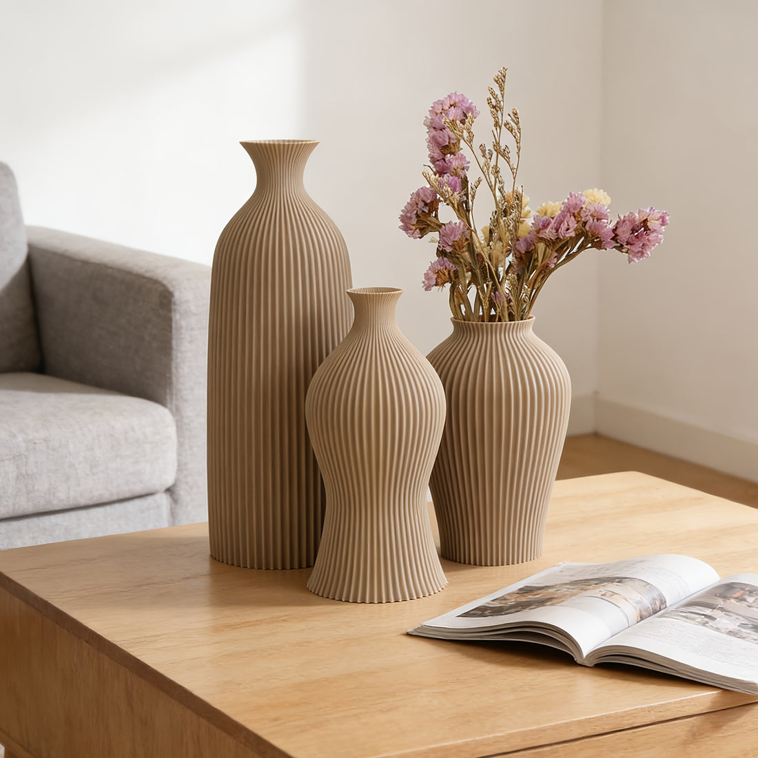 Three beige textured vases on a wooden table with an open magazine.