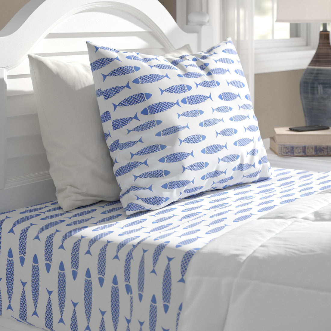 Bed with blue fish patterned bedding and pillow on a white bed frame.