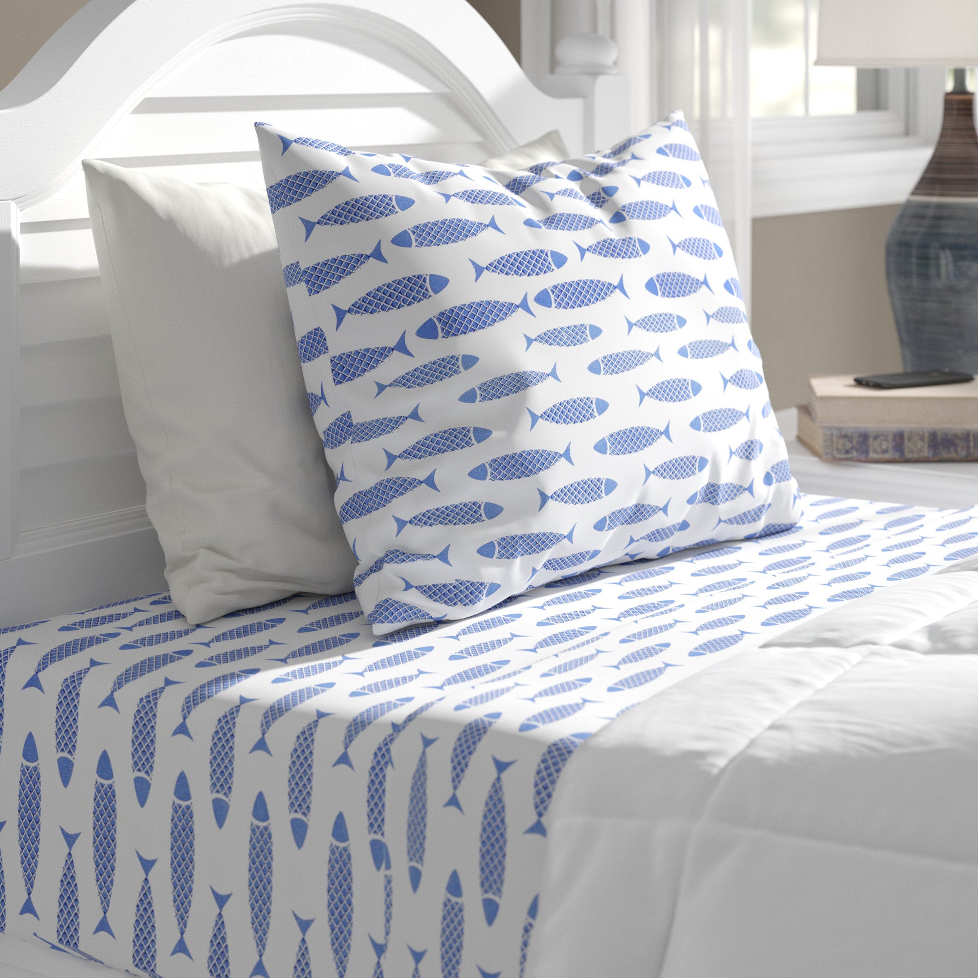 Bed with blue fish patterned bedding and pillow on a white bed frame.
