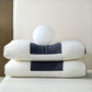 Two white pillows with black accents stacked on a bed against a neutral wall.