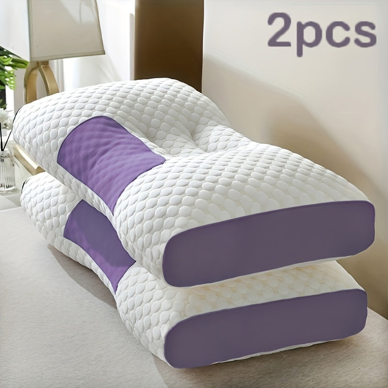Two white and purple pillows on a bed with a lamp in the background.