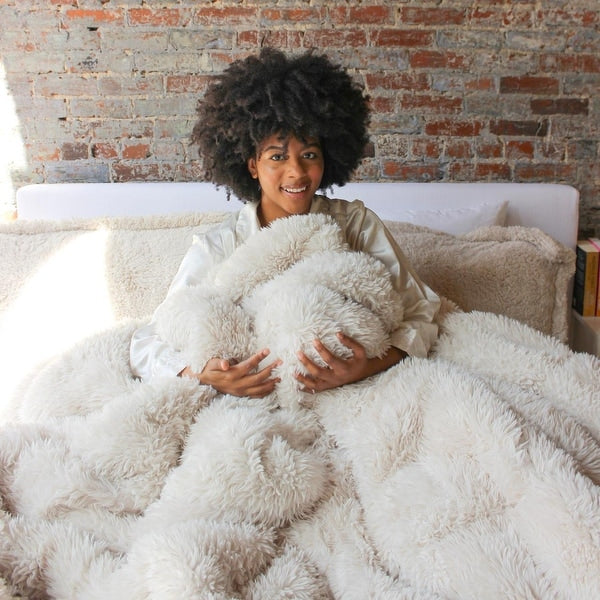 Woman holding a fluffy white pillow in front of a brick wall.