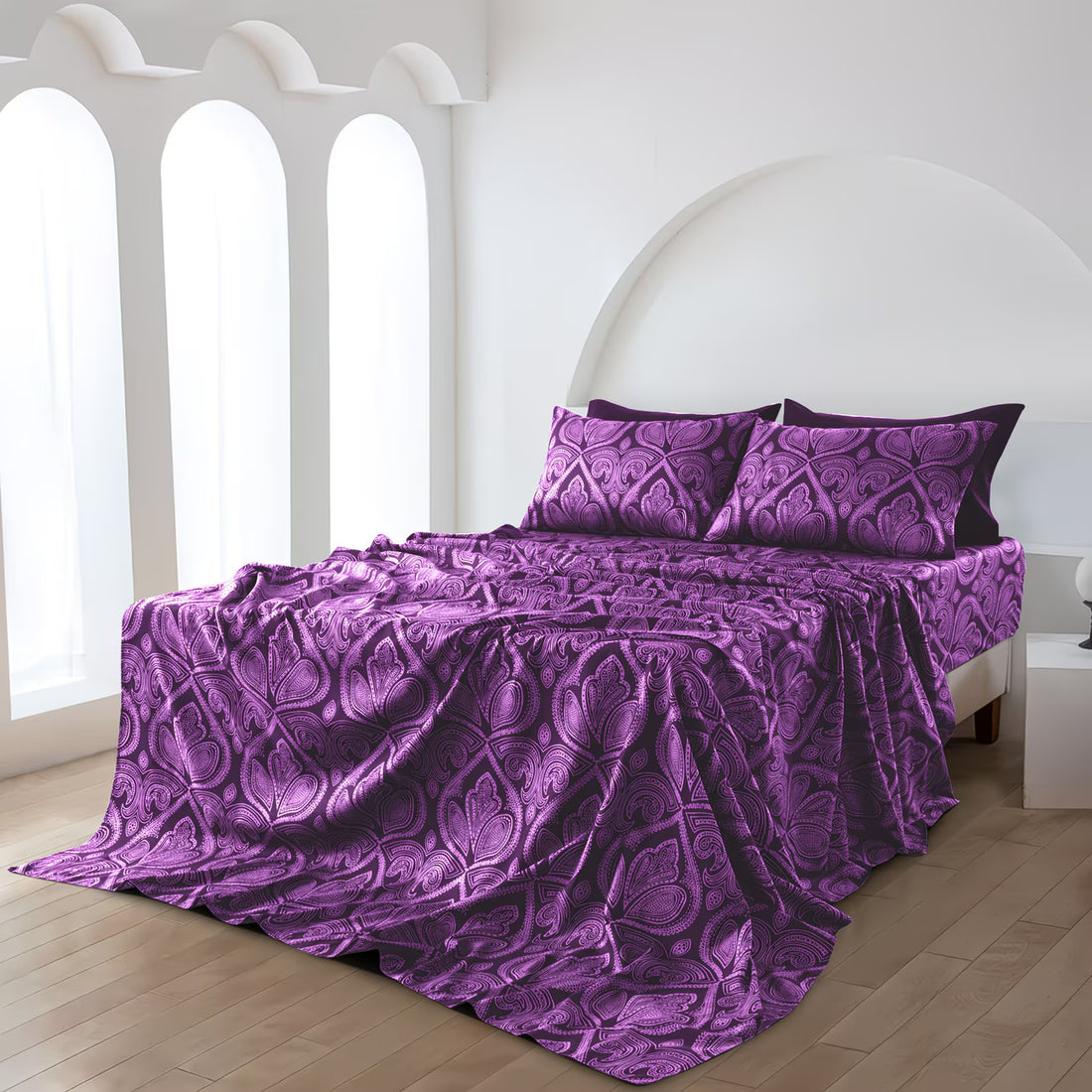 Purple patterned bedspread and pillows on a bed in a bright room.
