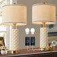 Two table lamps with beige lampshades and textured white bases on a wooden surface, with two light bulbs and a power adapter displayed.