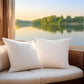 White pillows on a wicker chair with a scenic view of a lake and trees.