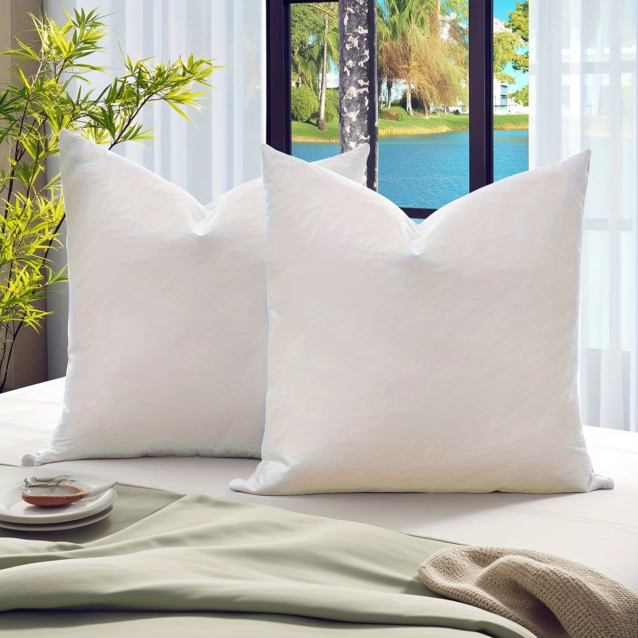 Two white pillows on a bed with a scenic view of a lake through a window.