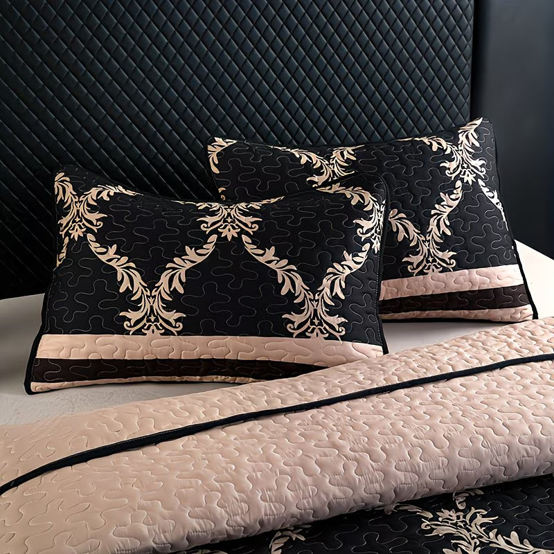 Decorative pillows with black and gold pattern on a quilted bedspread.