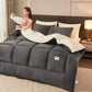 Woman lying in bed under a large gray comforter with a neutral color scheme.
