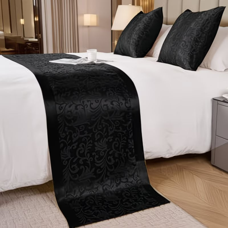 Decorative black runner on a bed with white bedding in a bedroom setting.