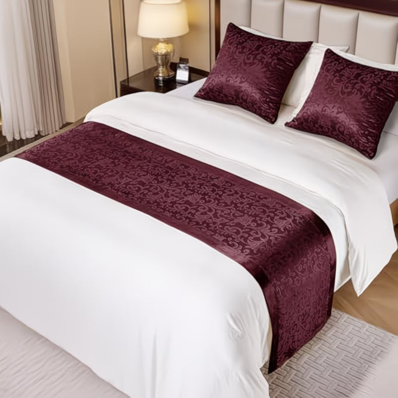 Bed with white bedding and burgundy decorative pillows and runner in a bedroom setting.
