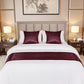 Neatly made bed with burgundy and white bedding in a well-lit bedroom.